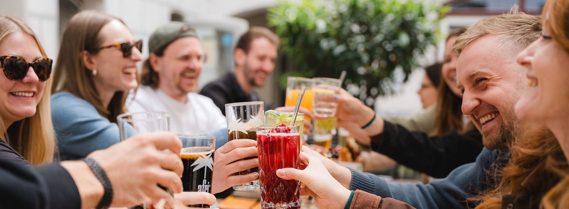 Gruppe junger Menschen sitzt bei Tageslicht an einem Tisch im Freien und unterhält sich lebhaft.