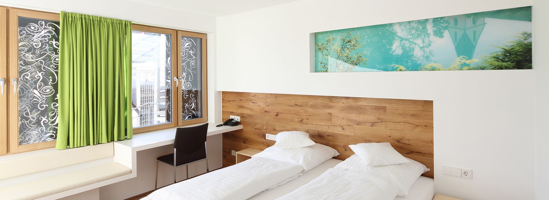 Modernes Doppelzimmer mit hellem Holz, großem Fenster und grünem Vorhang.