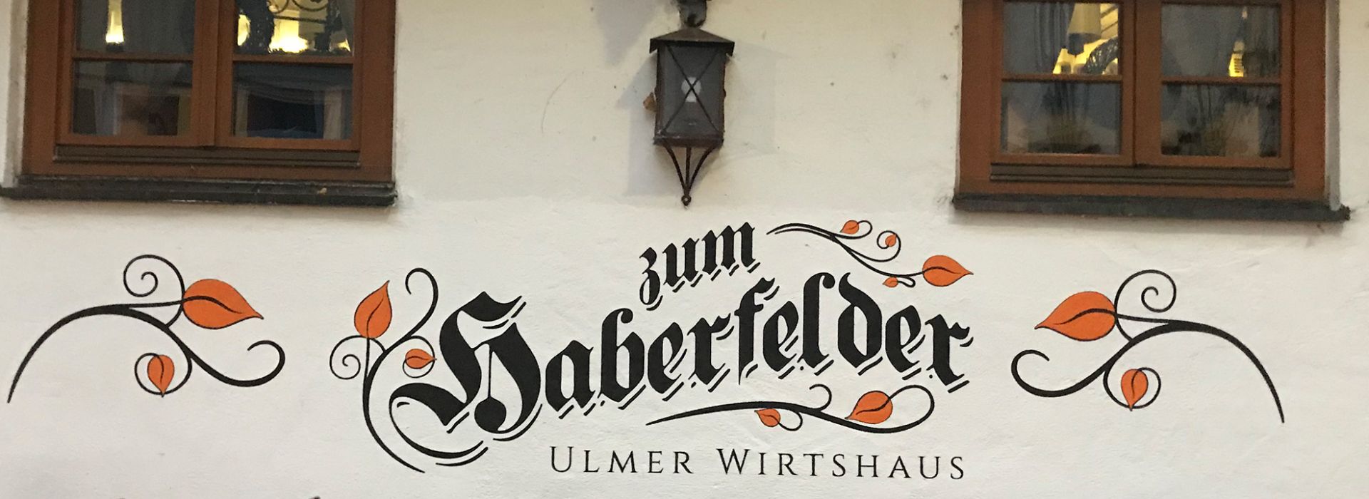 Schriftzug „Zum Haberfelder – Ulmer Wirtshaus“ in kunstvoller, traditioneller Typografie an einer weißen Hauswand, dekoriert mit geschwungenen Ranken und Blättern.