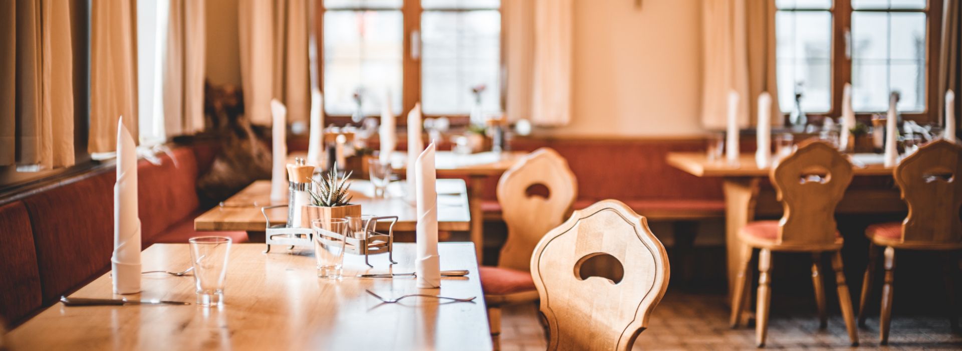 Nahaufnahme eines elegant gedeckten Tisches für eine Feier. Die Tafel ist mit weißen Stoffservietten, Kerzenleuchtern und kleinen Blumengestecken dekoriert.