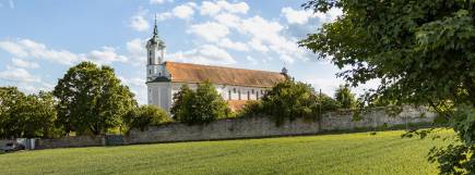 Landschaftsaufnahme mit großer Wiese und barocker Kirche, flankiert von Bäumen.